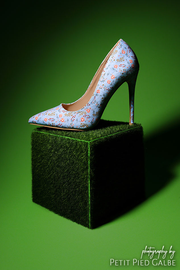 Blue high heeled shoe showcased on a green grass cube prop, in low key lighting.